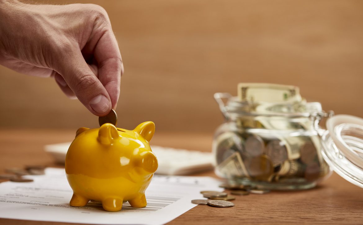cropped view of man putting coin in yellow piggy bank
