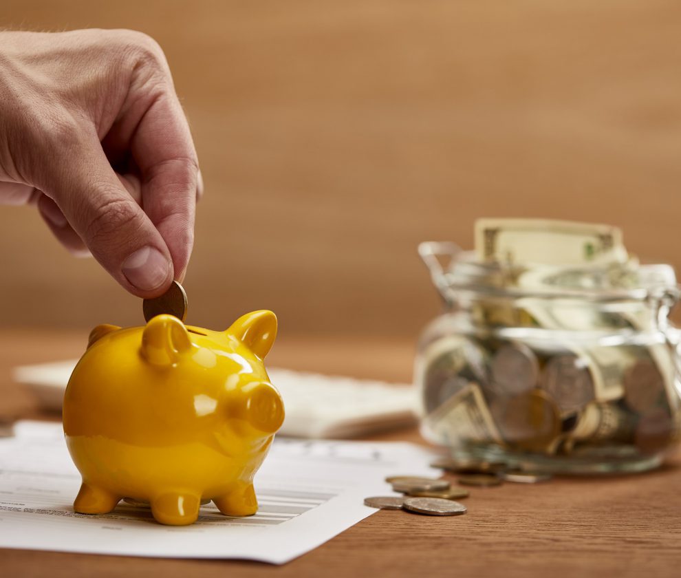 cropped view of man putting coin in yellow piggy bank